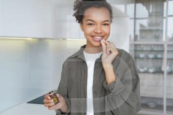 Radiant biracial girl smiles as she takes dietary supplements, vitamins, ensuring healthy skin and hair for a confident appearance.
