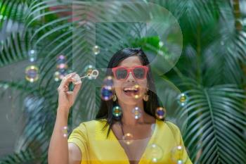 Front view of a cheerful Latina woman with bubbles in the air against a background of green plants outdoors.. Cheerful Latina woman with bubbles in the air against a background of green plants outdoors