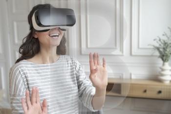 Young excited woman wearing 3d goggles interacting with augmented world, amazed female in VR headset playing games or making purchases in virtual reality store while spending leisure time at home. Young excited woman wearing VR headset interacting with augmented world, playing games at home