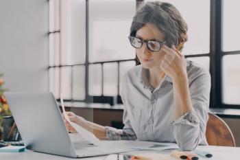 Young businesswoman in glasses feeling tired, suffering from eye strain and fatigue during computer work, overworked hispanic female employee working in front of laptop all day in office. Businesswoman in glasses feeling tired, suffering from eye strain and fatigue during computer work