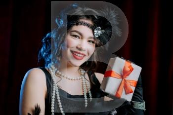Joyful vintage styled woman dressed in Art Deco era holding gift box with bow on velours background. She is glad to get present. retro, party, fashion concept. High quality photo. Joyful vintage styled woman dressed in Art Deco era holding gift box with bow on velours background. She is glad to get present. retro, party, fashion concept.