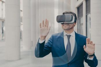 Professional architect in AR headset outdoors, gesturing and smiling, excited businessman using 3D goggles for work, moving virtual objects in air.