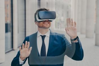 Excited businessman in suit on city street, testing VR glasses for the first time, gesturing and touching objects in air.