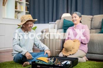 Asian couple old senior marry retired prepare luggage suitcase arranging for travel, Romantic retired couple packing clothes travel bag suitcase together on floor at home interior living room