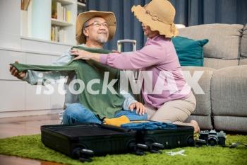 Asian couple old senior marry retired couple prepare luggage suitcase arranging for travel, Romantic retired couple packing clothes travel bag suitcase together on floor at home interior living room