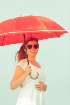 Beauty of ginger hair concept. Portrait of beautiful happy redhead adult plus size woman holding red umbrella wearing sunglasses in heart shape.. Portrait of redhead adult woman holding umbrella