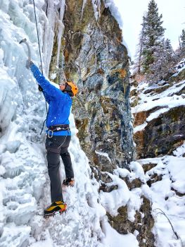 A climber climbs over an icy waterfall in winter. In the background, rocks and spruce