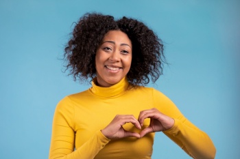 Kind african woman making sign of shape heart near her chest. Blue background. Women health, volunteering, donation help and love concept. High quality. Kind african woman making sign of shape heart near her chest. Blue background. Women health, volunteering, donation help and love concept.