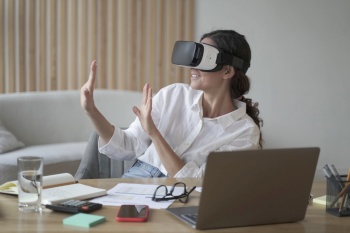 Happy woman exploring augmented world at work, touching 3d virtual objects with hands while sitting at office desk, excited female employee wearing vr headset, using virtual reality for business. Happy woman exploring augmented world at work, touching 3d virtual objects with hands