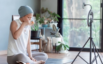 Asian cancer woman drinking tea while online video streaming at home. Health and Technology Concept.