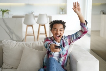 Excited football team fan is relaxing at home watching the game. African american teenage girl enjoying tv watching and shifts channels. Reality show or soccer match watching. Smart tv using.. Excited football team fan is relaxing at home watching the game. Soccer match watching.