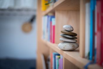 Feng Shui: Stone cairn at home in a book shelf, blurry books in foreground and background. Balance and relaxation.