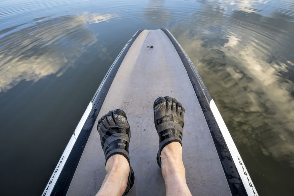 man feet in five finger water shoes on a stand up paddleboard
