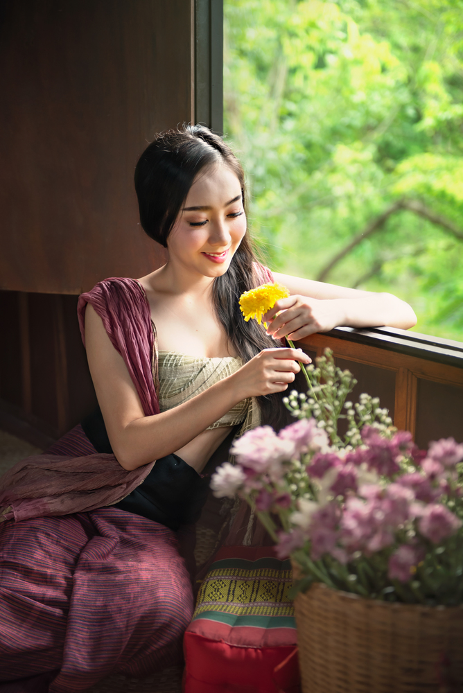 beautiful woman in traditional asian dresses holding flowers sitting near the windows. woman in traditional asian dresses