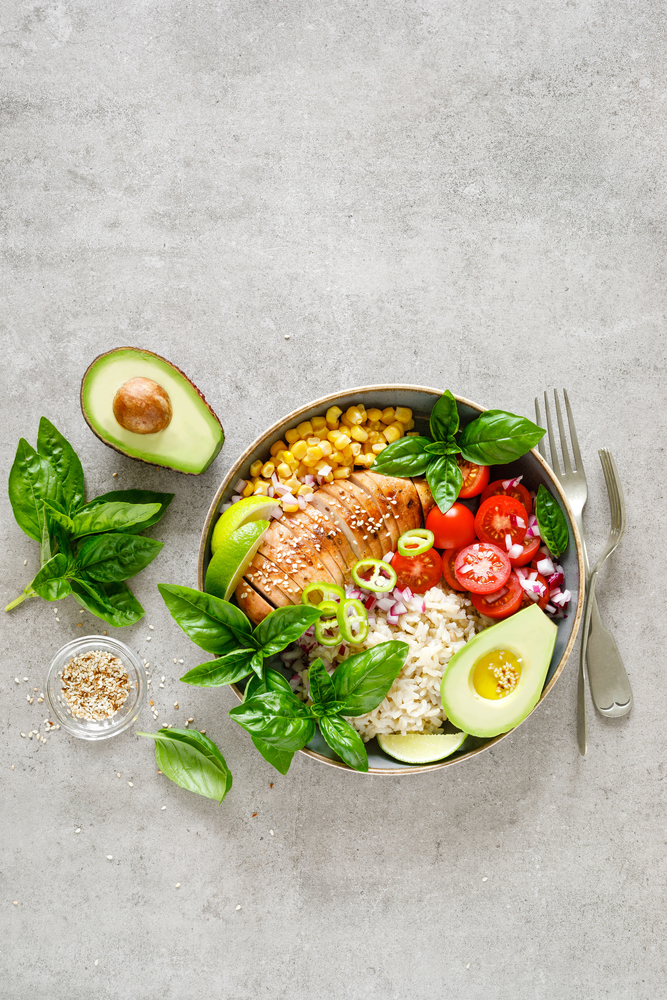 Buddha bowl with grilled chicken breast, tomato, onion, corn, avocado, fresh basil salad and rice, healthy balanced eating for lunch