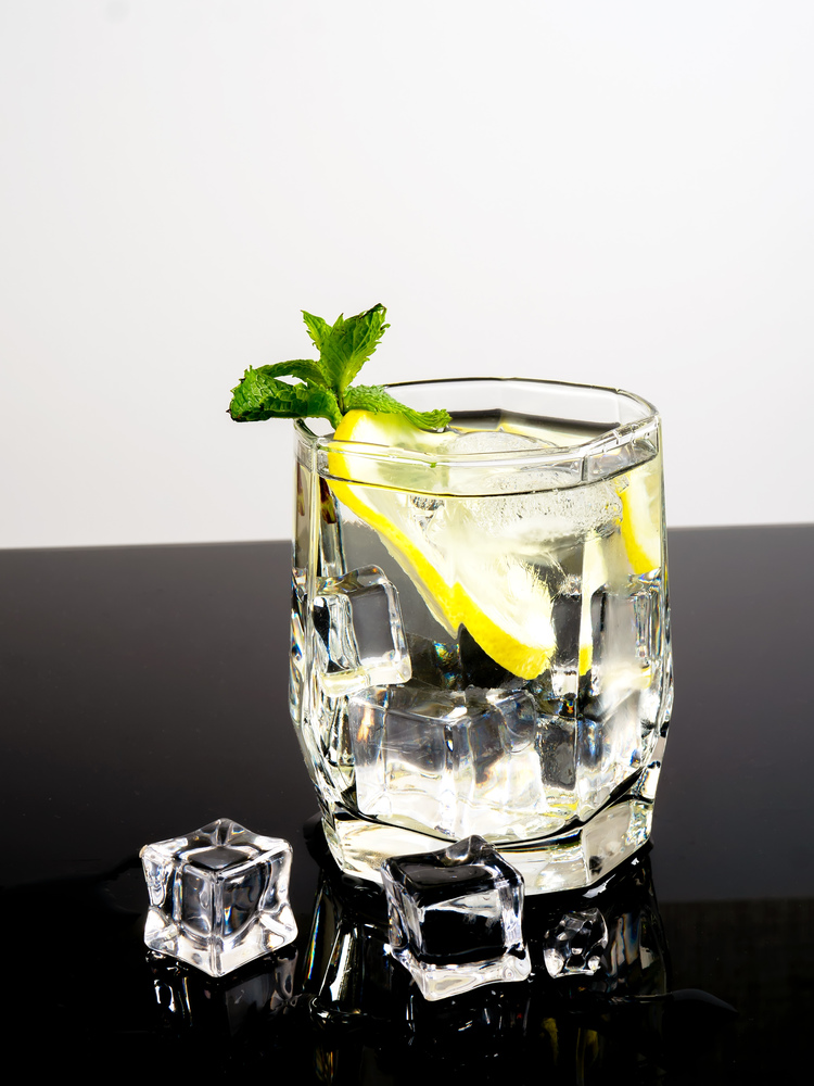 Glass with lemon vodka on a black background. Vodka with lemon and ice on a black background