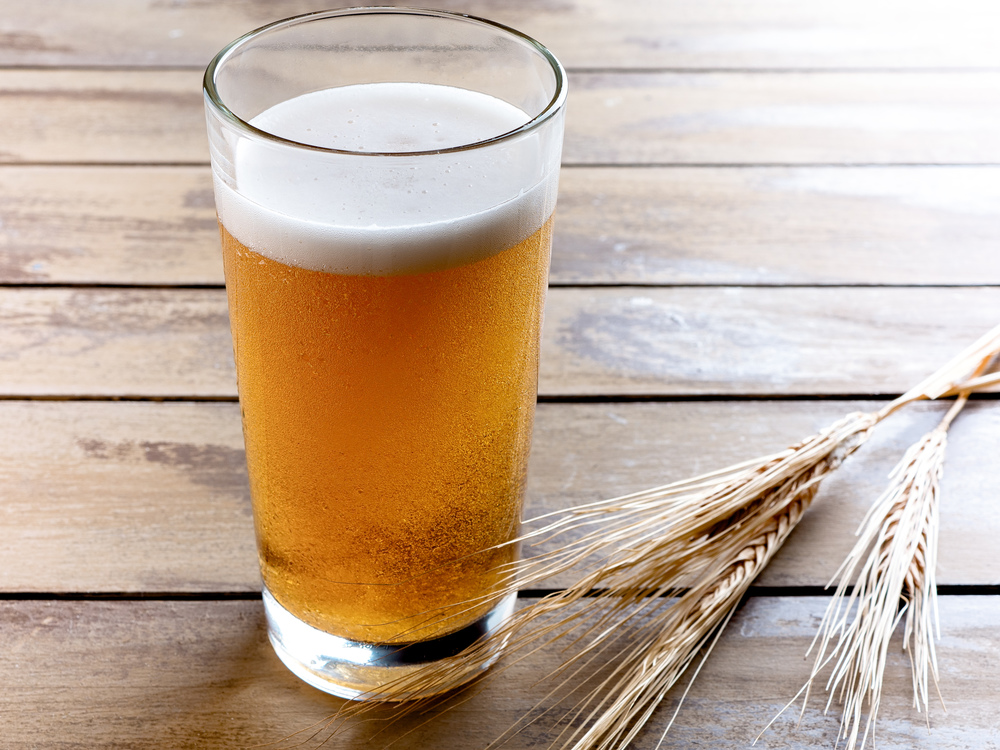 Glass of beer with ears of wheat on wooden background. Glass mug of beer on old wooden boards with ears of wheat on the background.