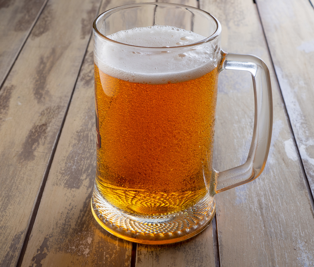 Mug of cold pale beer placed on a rustic wooden table. Mug of light beer on wooden boards