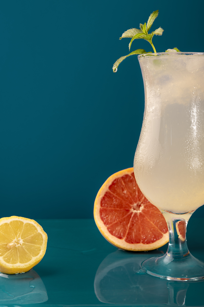 Lemon drink with ice and mint in a frosty glass. Refreshing soft drink with lemon and grapefruit slices on blue background