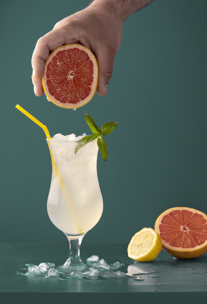 Summer drink with ice cubes, peppermint leaves and citrus fruits aroma. Grapefruits and lemons cold beverage in a glass against a blue background