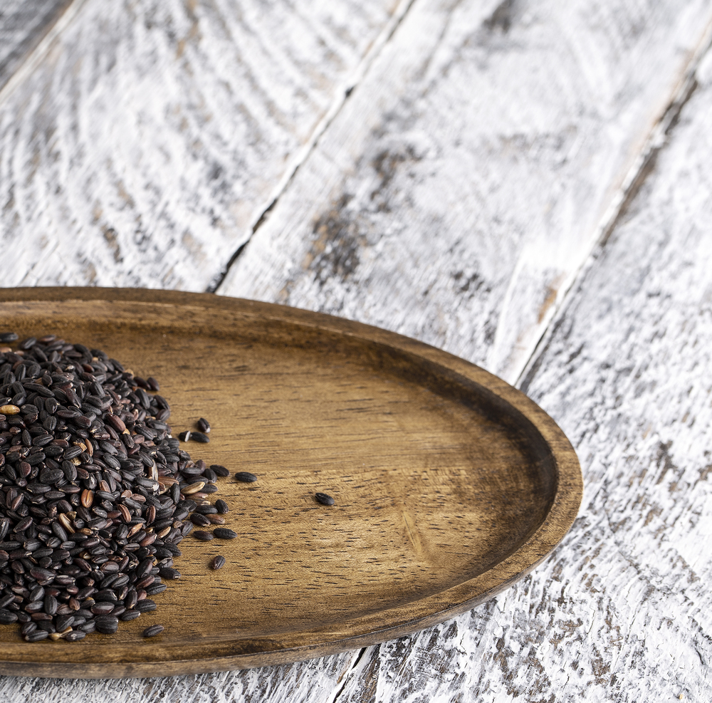 Wooden plate with black rice on old wooden background. The Wooden plate with black rice on old wooden background