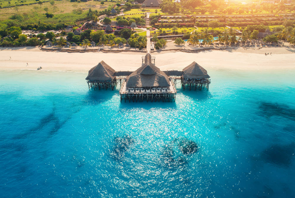 Aerial view of beautiful hotel in Indian ocean at sunset in summer. Zanzibar, Africa. Top view. Landscape with wooden hotel on the  sea, blue water, sandy beach, green trees, buildings. Luxury resort. Aerial view of beautiful hotel in Indian ocean at sunset in summer