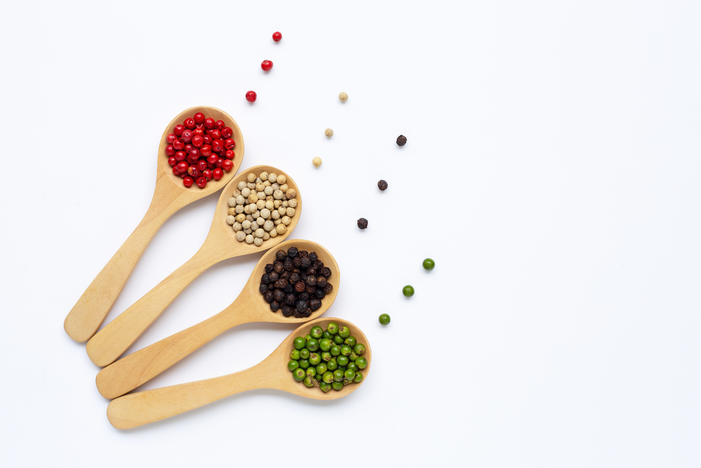 Green, red white and black peppercorns with wooden spoon on white background.