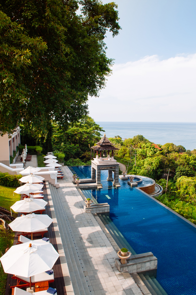 MAY 19, 2014 Krabi, THAILAND - Hill top pool under big tree with seascape, white umbrellas and sunbeds, Koh Lanta tropical resort outdoor space in summer