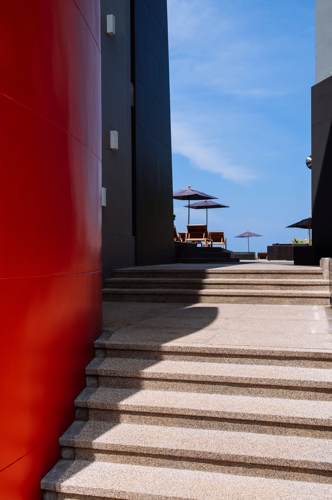 MAR 19, 2014 Koh Lanta, Krabi, Thailand - Modern exterior of hotel building with stairs and pool bed umbrellas in distance. High contrast light and shadow on building wall in summer time