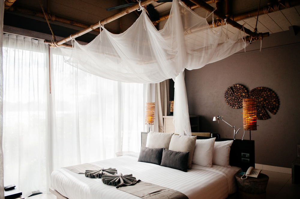 MAY 21, 2014 Krabi, THAILAND - Asian Thai tropical luxury resort room with wooden bed and white curtain and bamboo floor lamps. High ceiling hotel room interior.