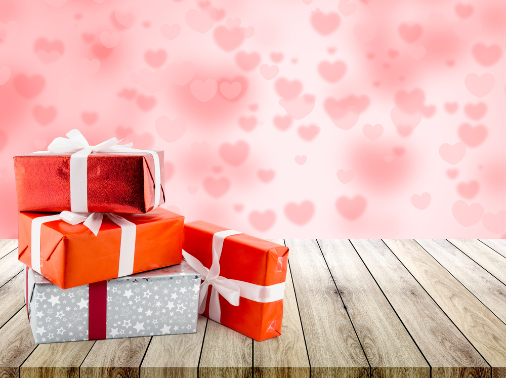 Red gift box and heart shape on wood table top with heart blur bokeh background, valentines day concept.