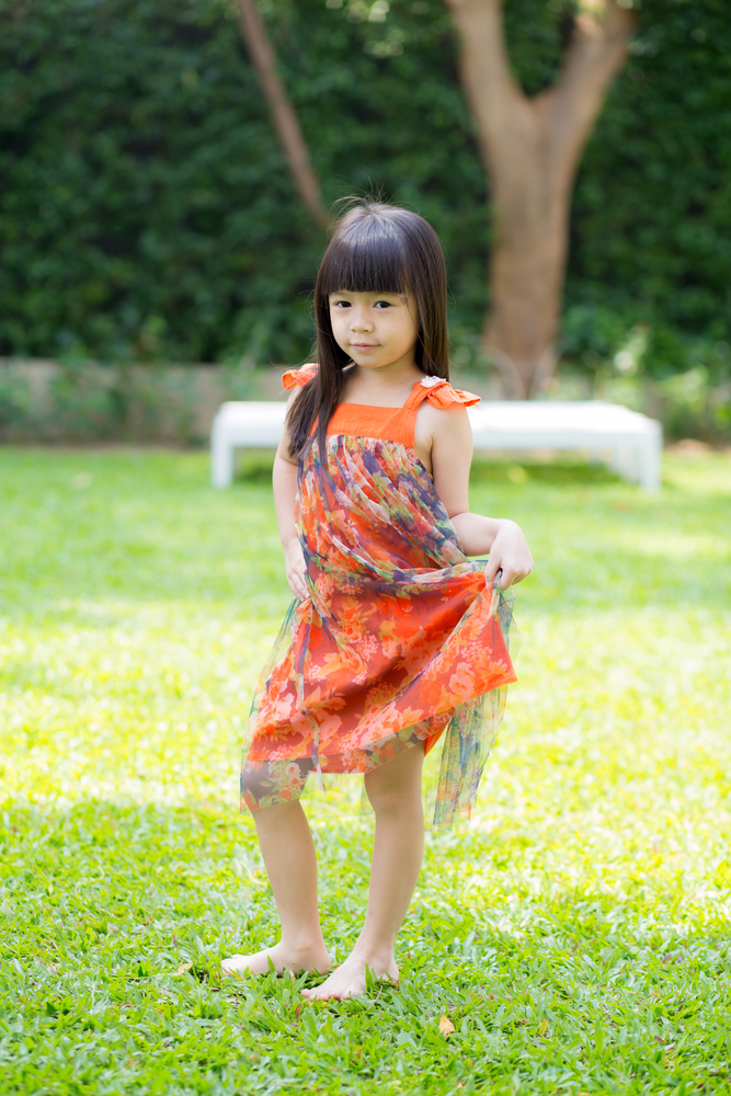 Beautiful portrait little girl asian of a smiling standing on green grass at the park, kid leisure and joyful in outdoor.