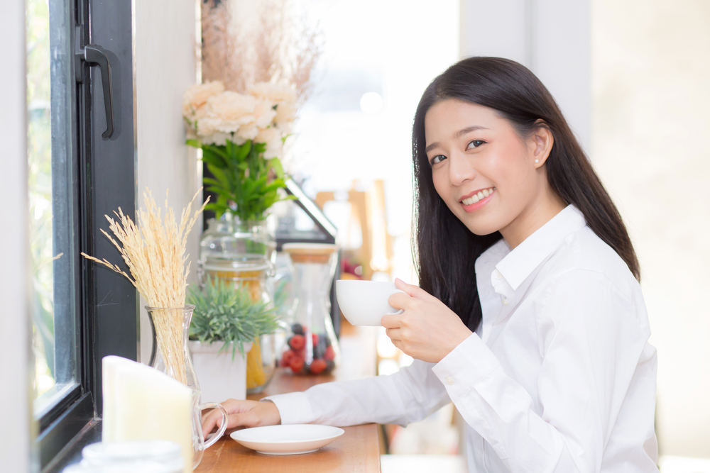 Beautiful  young asian woman drinking coffee and smile in the morning at cafe, girl sitting in coffee shop for breakfast and leisure during free time.