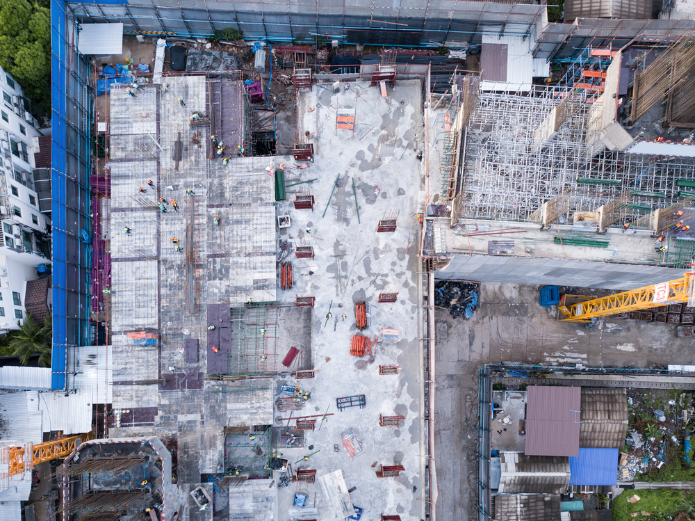 Aerial view of busy industrial construction site workers with cranes working. Top view of development high rise architecture building at noon.