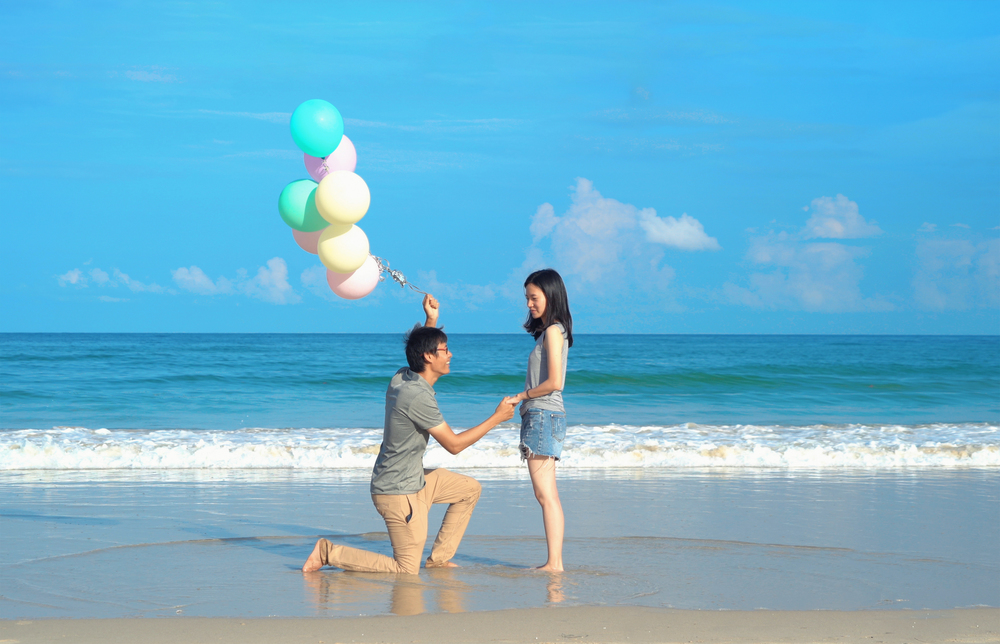Happy Asian couple holding colorful balloons at the beach during travel trip on holidays vacation outdoors at ocean or nature sea at noon, Phuket, Thailand