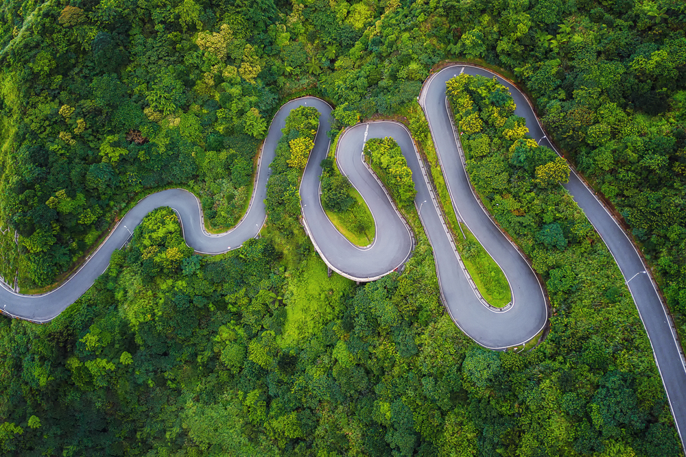 Aerial view of cars driving on curved, zigzag road or street on mountain hill with green natural forest trees in rural area of New Taipei City, Taiwan