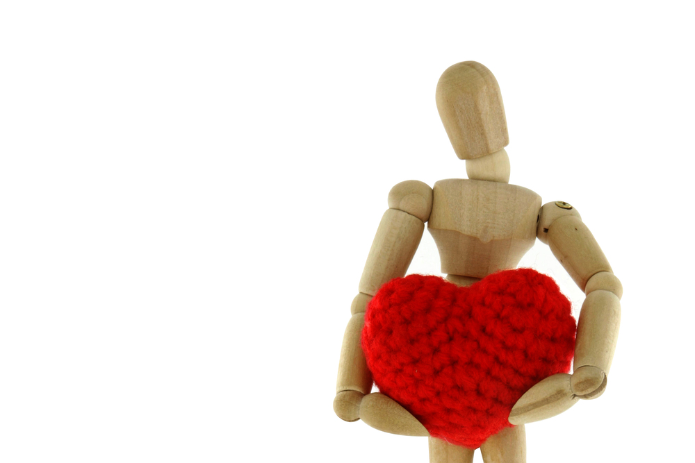 Wooden mannequin holding heart knit with yarn, isolated on white background