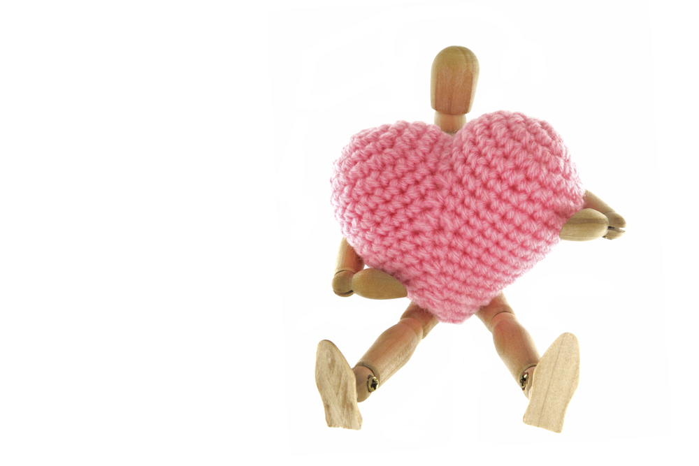 Wooden mannequin hugging heart knit with yarn, isolated on white background