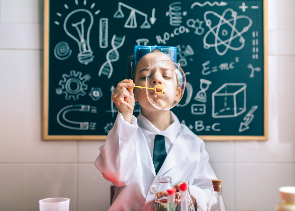 Little boy scientist playing with soap bubbles against of drawn blackboard. Kid doing soap bubbles against of drawn blackboard
