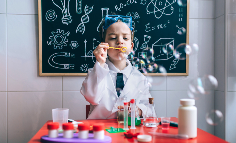 Little boy scientist playing with soap bubbles over table against of drawn blackboard. Kid doing soap bubbles against of drawn blackboard