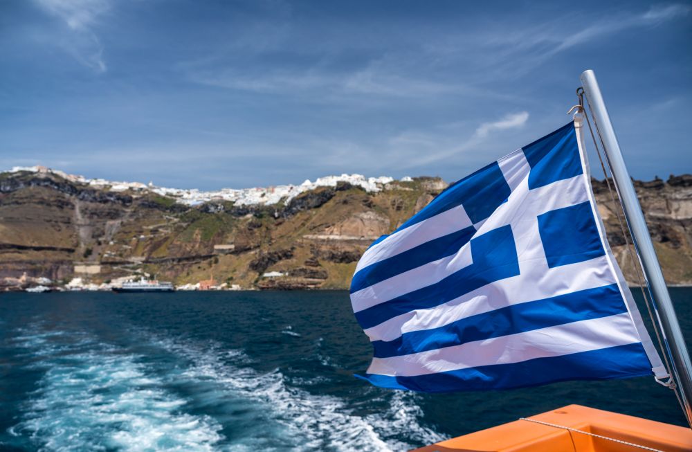 Greek flag on tender boat leaving Fira port on Santorini. Fira port on  volcanic caldera island of Santorini