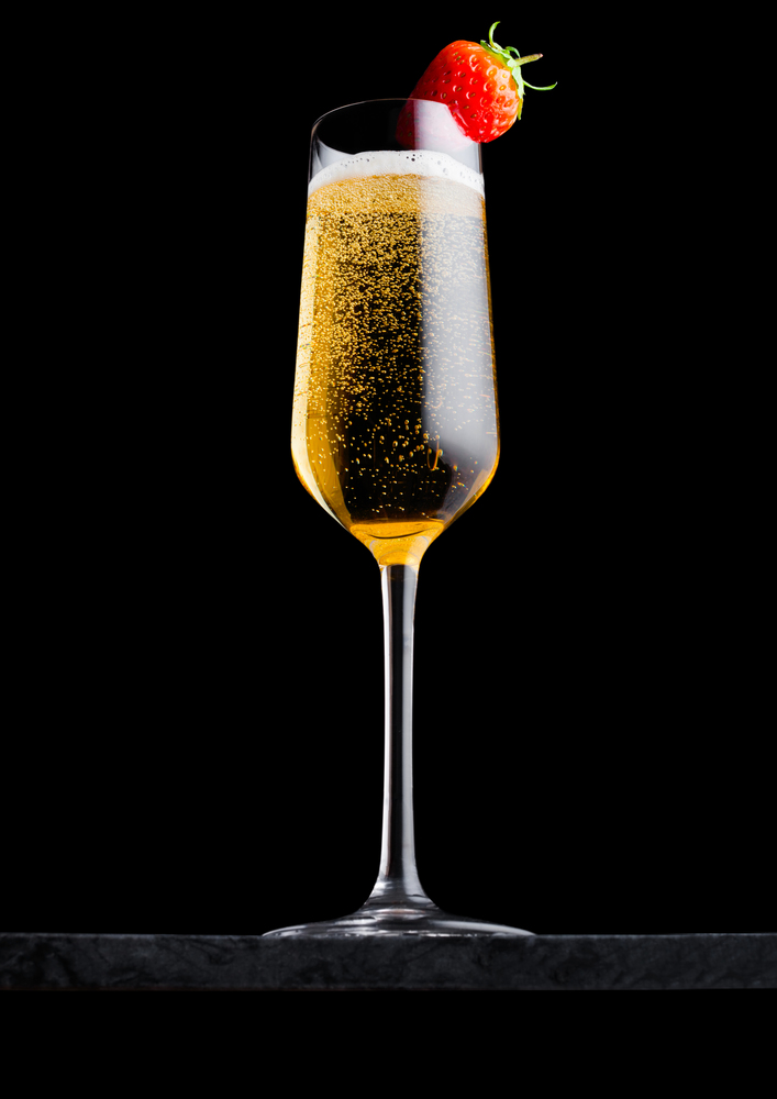 Elegant glass of yellow champagne with strawberry on top on black marble board on black.
