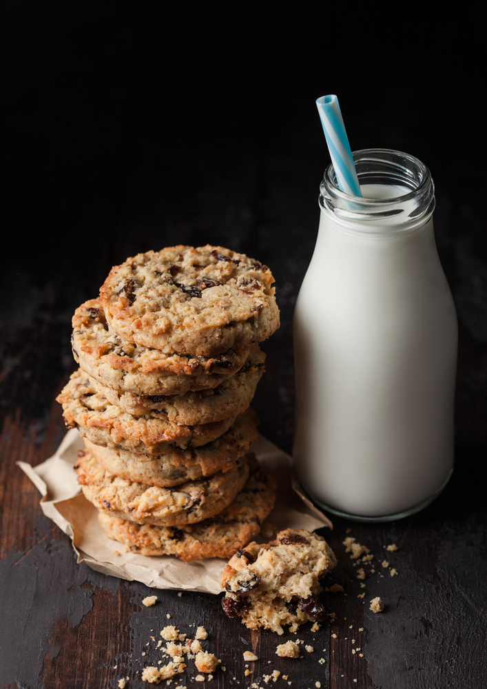 Homemade organic oatmeal cookies with raisins and apricots and bottle of milk on dark wood background.