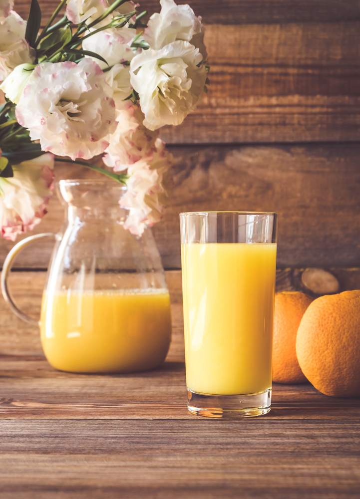 Glass of orange juice with fresh oranges on the wooden background