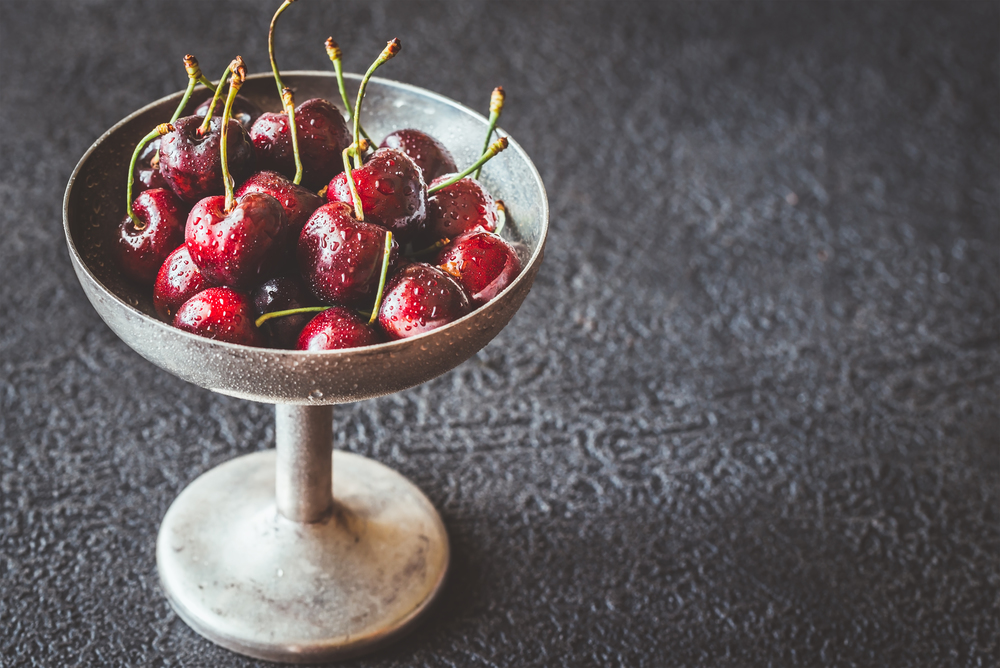 Fresh cherries in vintage silver vase on the dark wooden background