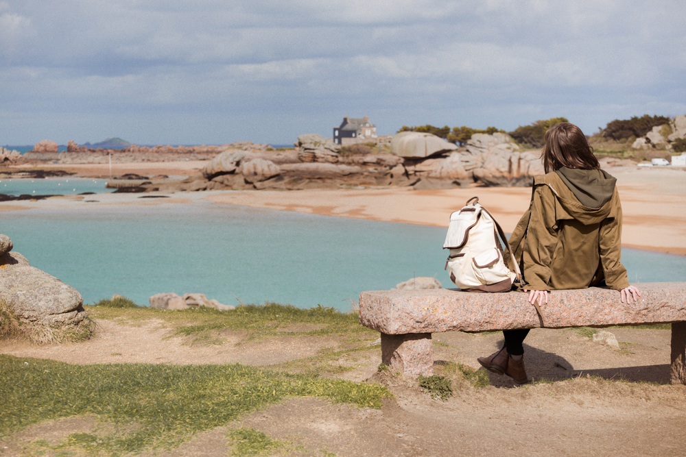 girl traveler sits on a bench near the sea and the shore at  the Tregastel, Brittany. France