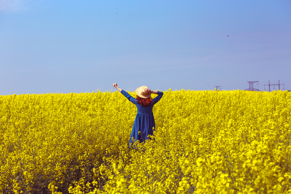 Happy girl in a hat walking in amazing field of yellow rapeseed in the countryside. Emotions