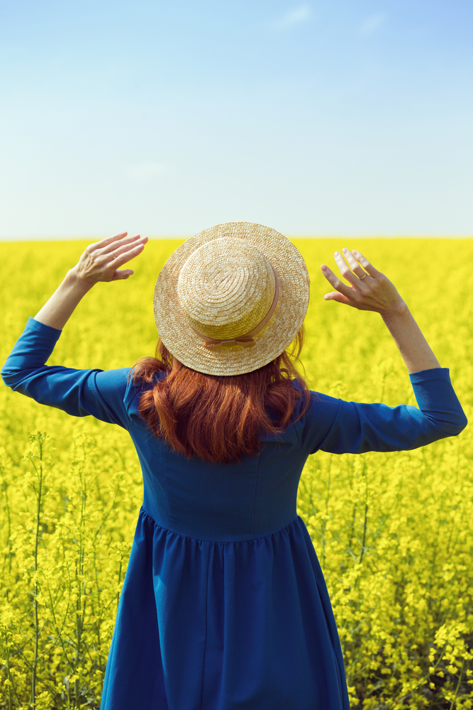 Happy girl in a hat walking in amazing field of yellow rapeseed in the countryside