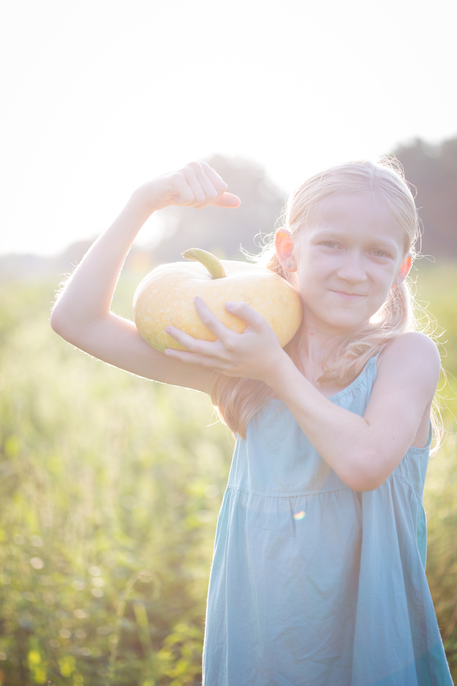 summer vacation of a little girl in the village. Fun girl with pumpkin in the garden at sunset