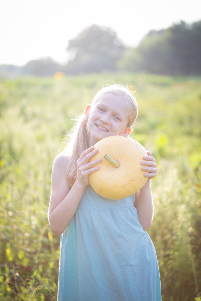 summer vacation of a little girl in the village. Fun girl with pumpkin in the garden at sunset